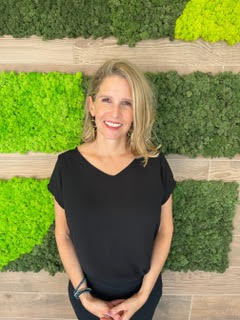 Portrait of Julie D. Gruber, LMFT, smiling in front of a green living wall